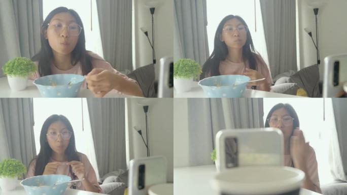 亚洲女孩在家里吃午饭时，通过智能手机观看病毒视频和跳舞，生活方式概念。