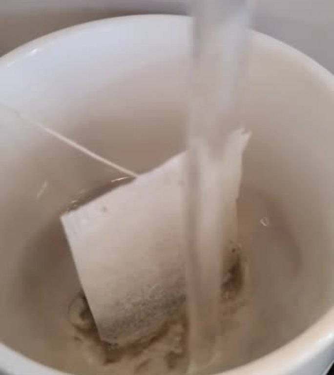用茶包将热水倒入白色杯子的镜头
