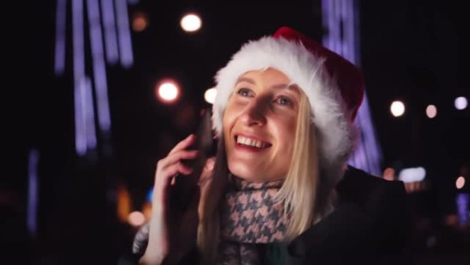 一个戴着圣诞老人帽子在智能手机上聊天的女人是一个夜城。