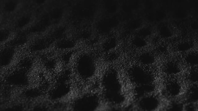 带有酒窝的黑砂表面。深色沙滩的单色纹理背景。火药，颗粒粉尘