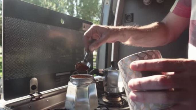 在一个阳光明媚的早晨，双手将咖啡倒入露营车中的意大利moka咖啡机中的特写镜头