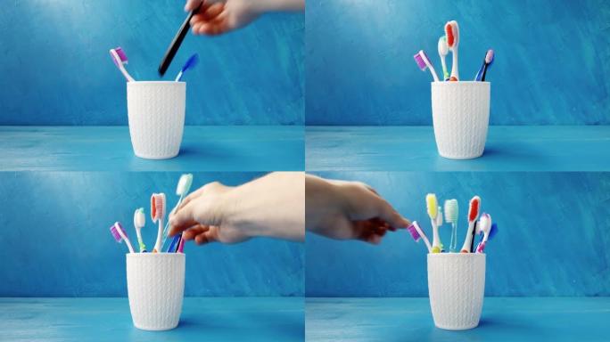 一只手将不同的多色牙刷放入蓝色背景上的杯子特写镜头中。4k原始视频。