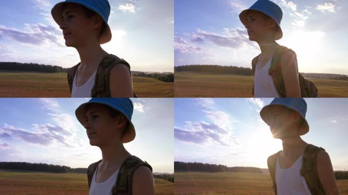 带着背包的青少年男孩旅行者在夏天的日落时分穿过田野，在一座小山的山顶上，steadicam拍摄
