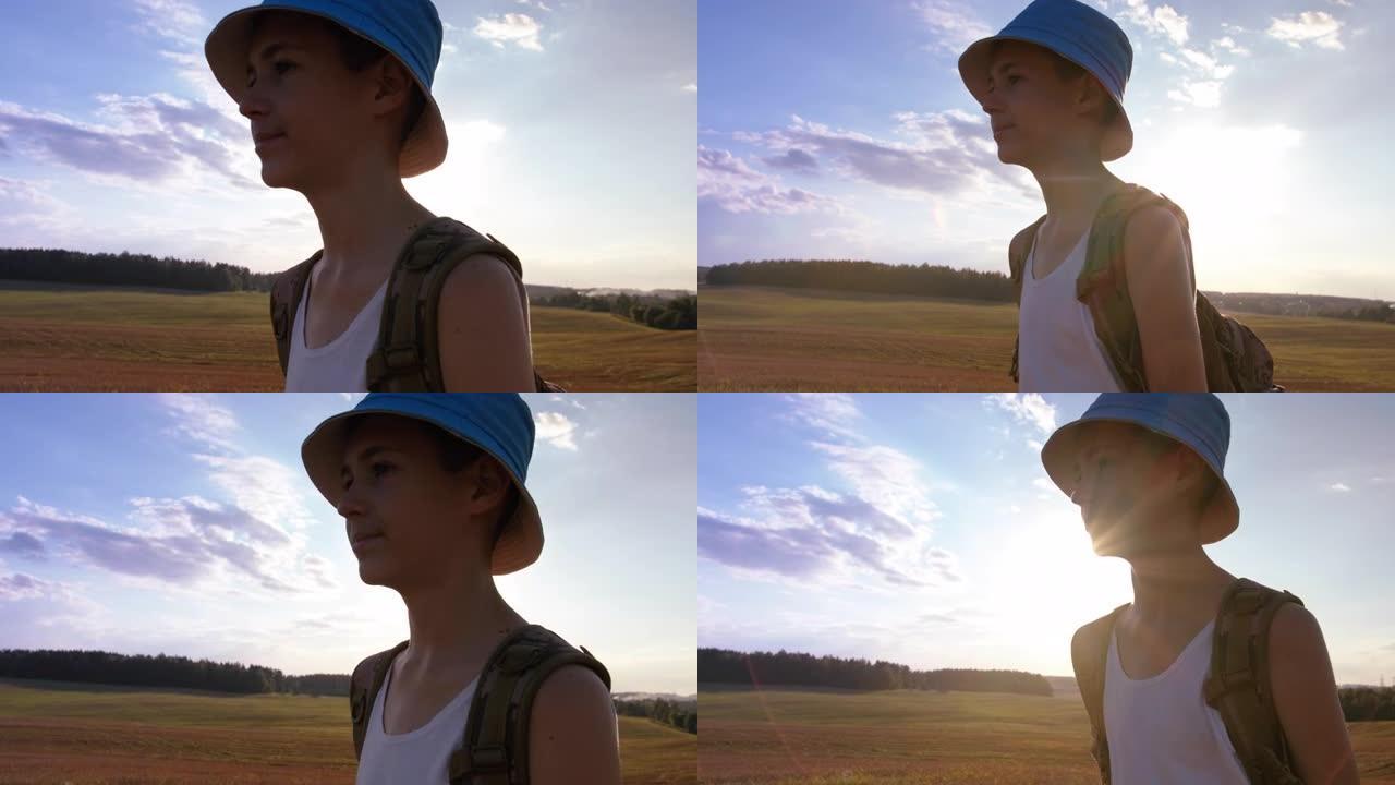 带着背包的青少年男孩旅行者在夏天的日落时分穿过田野，在一座小山的山顶上，steadicam拍摄