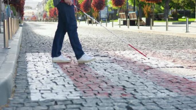 一个盲人拄着拐杖过马路。年轻盲人在户外独自行走时使用安全棍