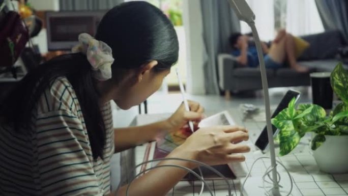 亚洲女孩在家里的餐桌上做作业时使用数字平板电脑和铅笔，生活方式理念。