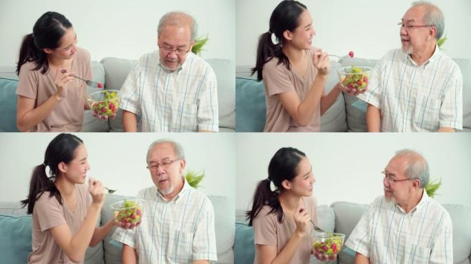 照顾者年轻的亚洲妇女喂养蔬菜老年亚洲男子坐在家里的客厅沙发上。女治疗师正在监测老年男性患者的症状。医