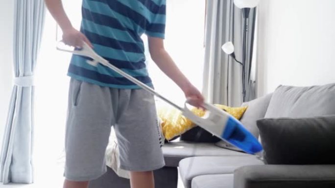亚洲男孩正在家里用吸尘器吸尘窗户附近的沙发，周末活动生活方式。