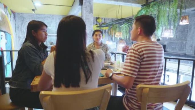 一群快乐的年轻人在餐馆吃饭，互相交谈。
