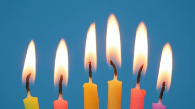 在蓝色背景的生日蛋糕中点燃蜡烛。在自制蛋糕中关闭彩色火焰蜡烛。家庭聚会的生日蜡烛