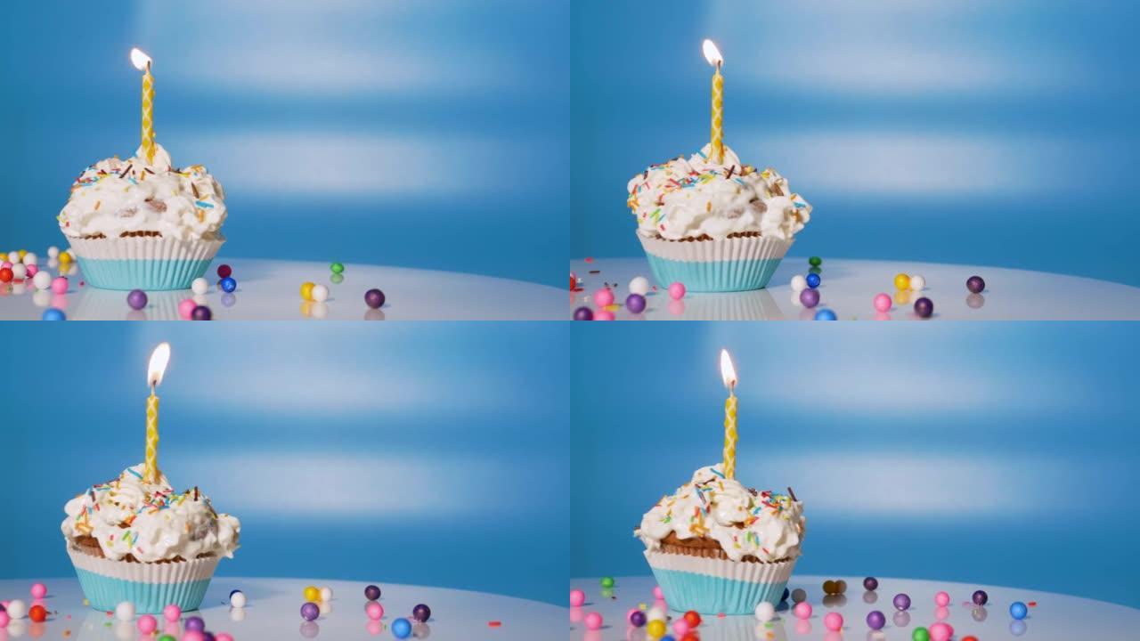 唱盘上放着节日奶油蛋糕。给孩子的美丽的生日问候，生日纸杯蛋糕上有蜡烛和蓝色背景装饰。本空间