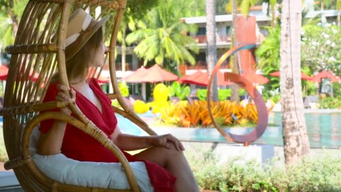 美丽的女性游客在豪华酒店的藤茧摇椅上放松