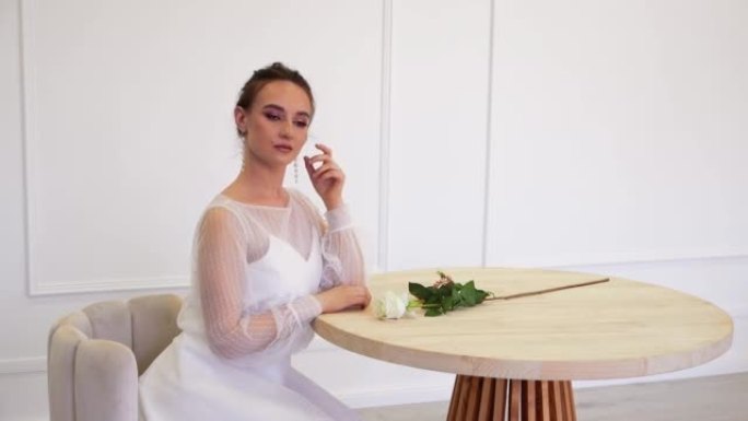 一个穿着白色婚纱的漂亮女孩靠在桌子上摆姿势。