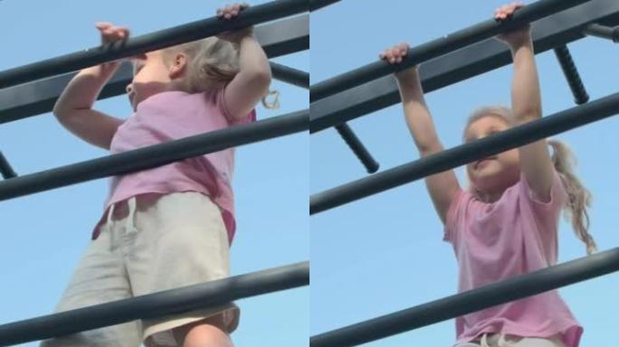 垂直视频: 小女孩在外面的露天运动场上爬上体操梯子。可爱的小女孩在太阳日在城市公园的垂直运动梯子上爬
