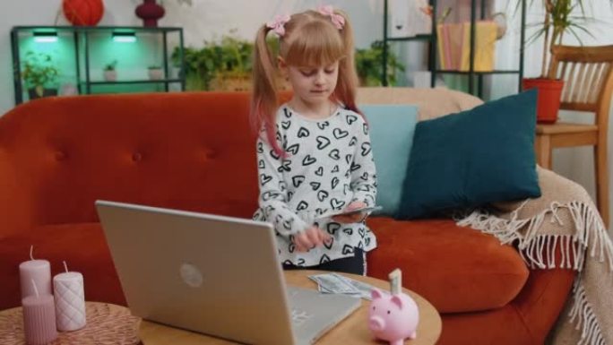 小女孩在家里用笔记本电脑、存钱罐数钱美元钞票满足未来的需求