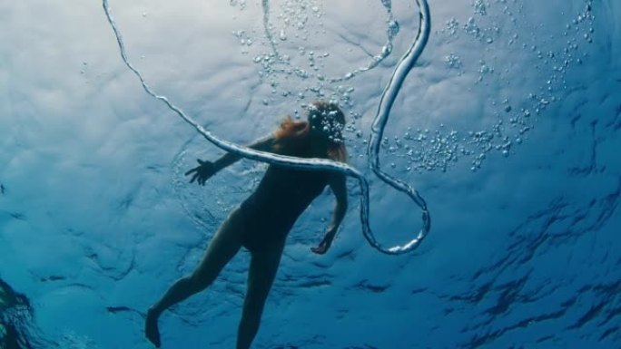 女人在水下游泳，看着环形气泡向水面移动