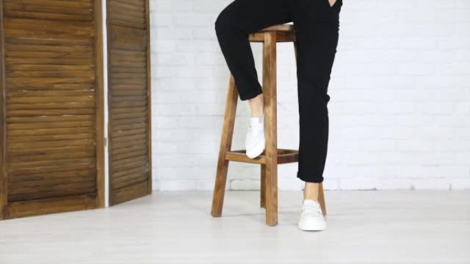 女孩模特爬上高高的木凳，把鞋子放在脚凳上。白色新型现代鞋类演示。白色墙壁背景。