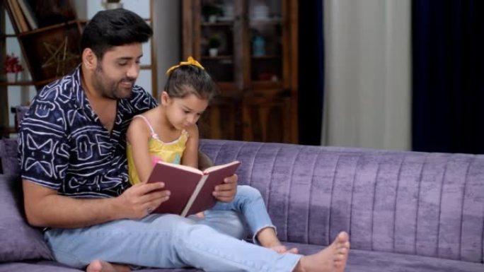 一个可爱的小女孩坐在父亲的腿上读故事书-快乐的育儿，一本有趣的书