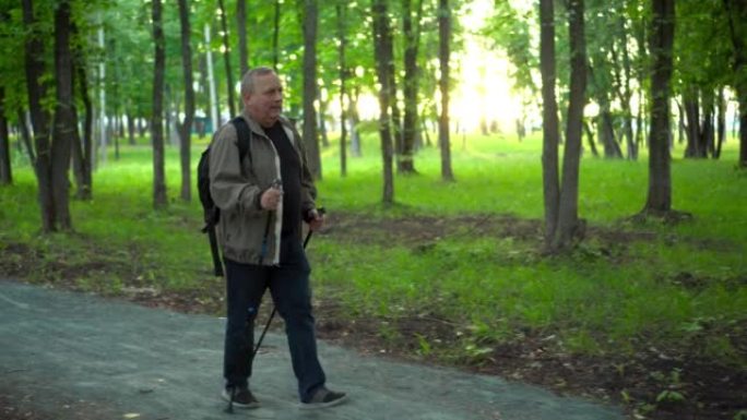 一位老人在森林中从事北欧行走。一个肩膀上背着背包的老人走路时，手里拿着棍子，以改善健康状况。