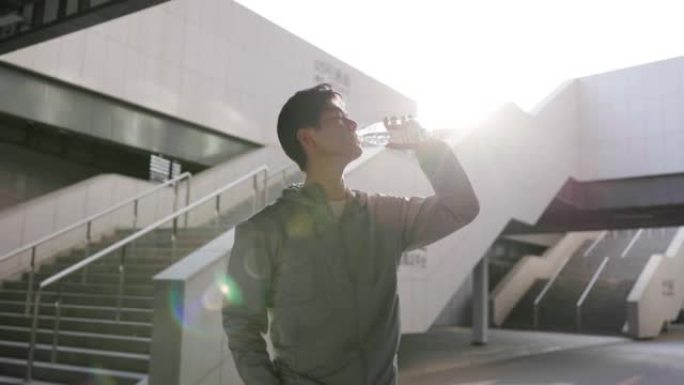 亚洲青年男子运动后在阳光下喝水