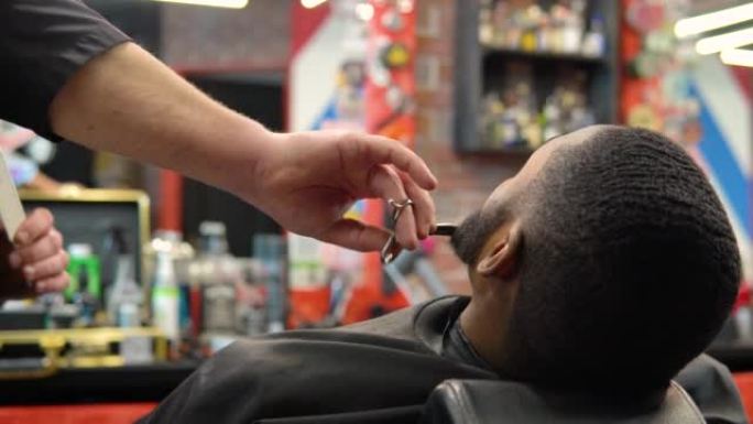 美发师用剪刀剪，用梳子梳客户的胡子。胡须护理。男人的美