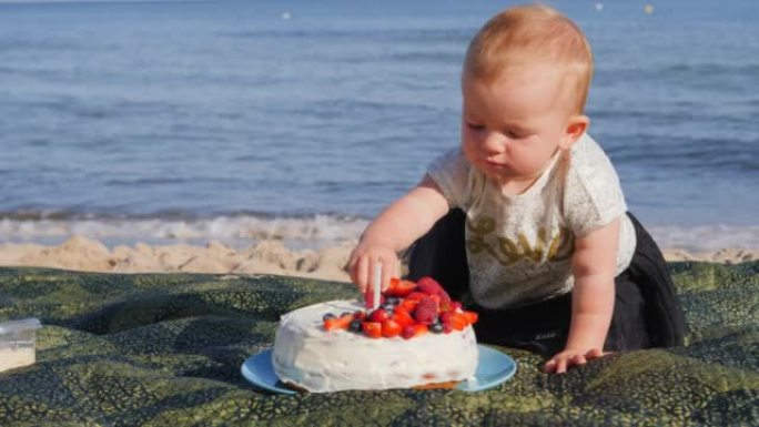 在海边为婴儿蹒跚学步的女孩庆祝一岁生日，地毯上放着甜蛋糕和蜡烛