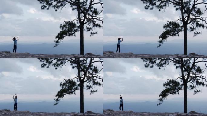 ฺ男孩高举双臂站在悬崖顶上。