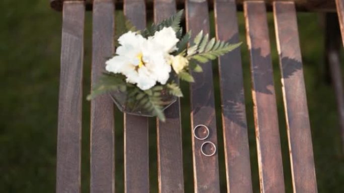 带花的花瓶站在棕色的木板条上，结婚戒指放在旁边