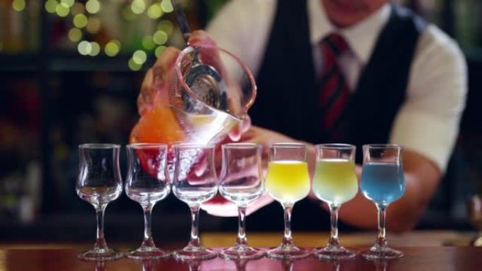 4k男调酒师在夜总会的酒吧柜台为顾客准备彩色鸡尾酒饮料。