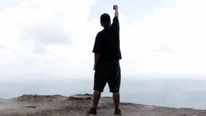 一个人高举双臂站在悬崖上。