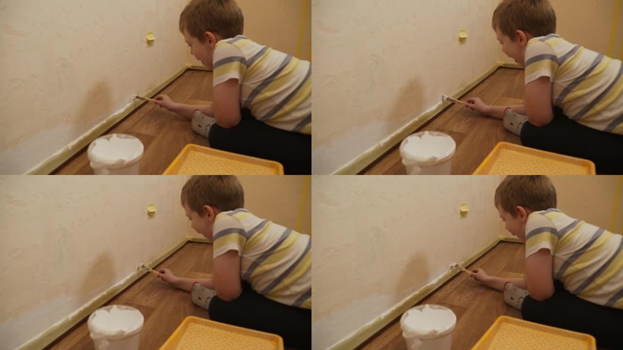 高加索男孩坐在地板上，在踢脚板附近用刷子粉刷墙壁
