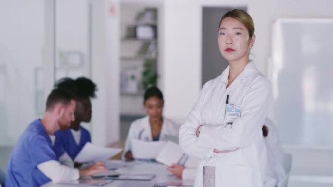 一位自信的亚洲医生在医院会议室开会时双臂交叉站着的肖像。专注的医生领导着一支由杰出和值得信赖的医生组
