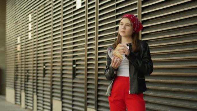 十几岁的女孩孩子走在城市街道上，边走边吃美味的三明治