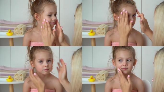 母亲给女儿脸上涂上奶油。洗澡后的孩子。婴儿护理，保湿霜