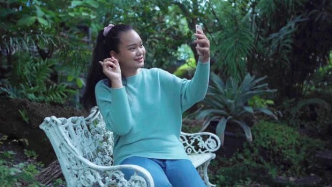 年轻的亚洲旅游女性在花园里使用智能手机进行自拍和广播，