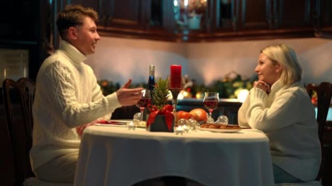 侧视图快乐相爱的成年夫妇坐在餐桌上微笑着交谈。积极的男人和女人在家里的厨房里约会。浪漫和情人节概念。