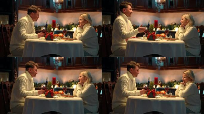 侧视图快乐相爱的成年夫妇坐在餐桌上微笑着交谈。积极的男人和女人在家里的厨房里约会。浪漫和情人节概念。