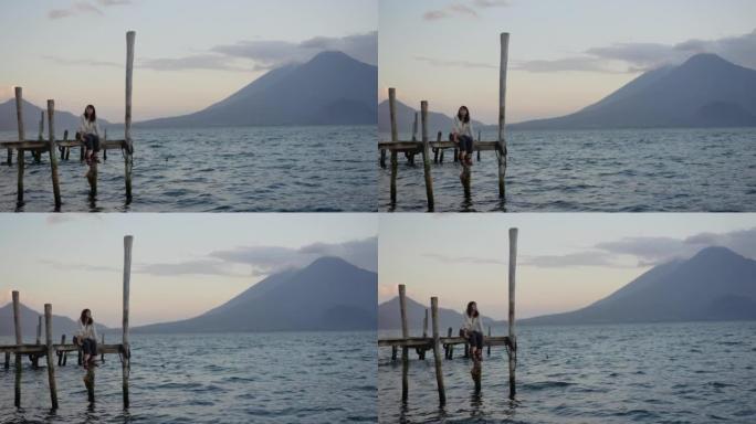 日落时坐在危地马拉阿蒂兰湖码头上的女人