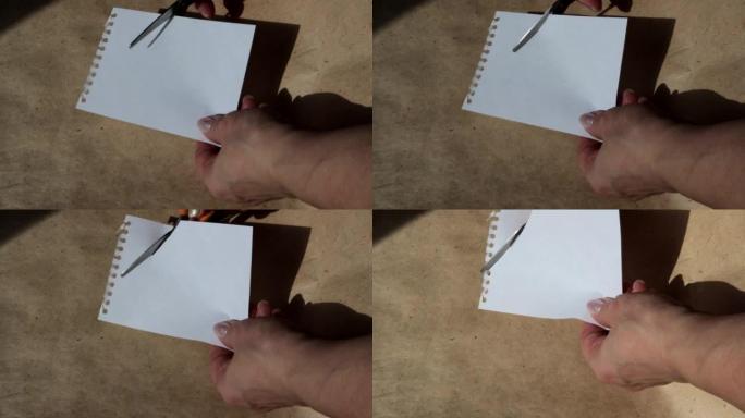 4k视频，一个女人的手在棕色牛皮纸的背景上用剪刀剪了一张空的白色纸