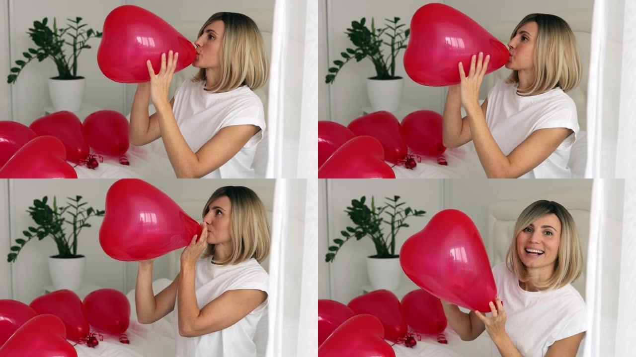 兴奋的女孩在床上给红心气球充气。女人在情人节欢喜礼物。随和的金发女孩在情人节表达积极的情绪。