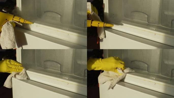 用黄色手套关闭无法辨认的男性家庭主妇的手，用蒸汽清洁器清洁空冰箱，用布洗架子做家务。