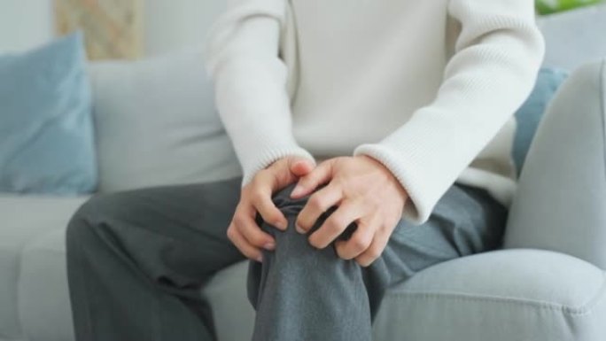 亚洲老年男子腿部受伤感到疼痛和痛苦。迷人的成熟男性患者坐在家里的客厅沙发上时膝盖有问题。医疗保险概念