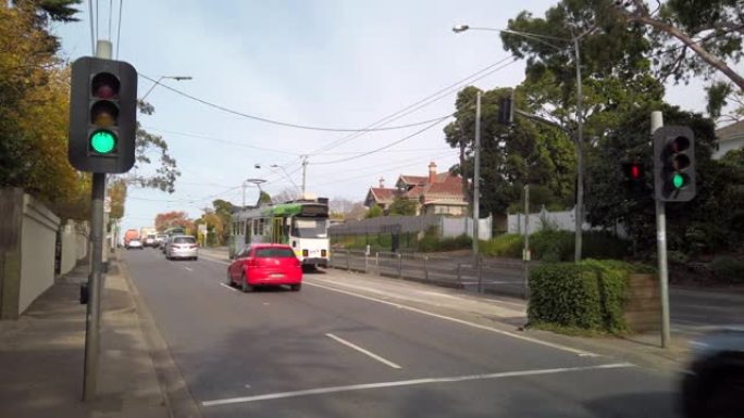 一辆电车从郊区的电车站出发，旁边是一条繁忙的道路上的交通，穿过绿色的交通信号灯。