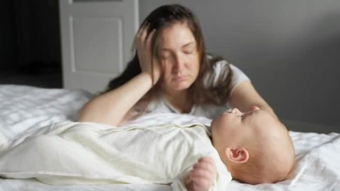 疲倦的母亲坐在哭泣的女婴附近的地板上睡觉