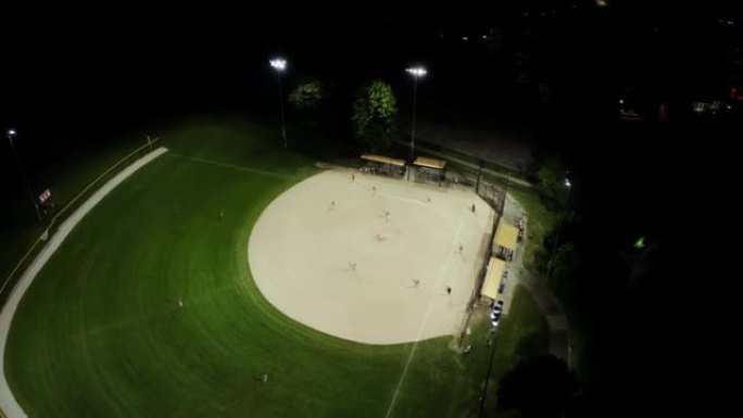 晚上棒球场的空中无人机镜头，人们在草地上打棒球。宽镜头