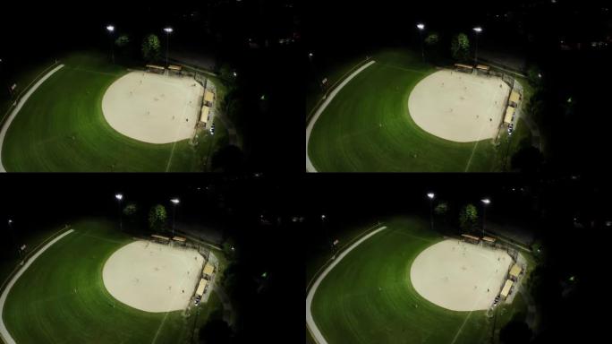 晚上棒球场的空中无人机镜头，人们在草地上打棒球。宽镜头