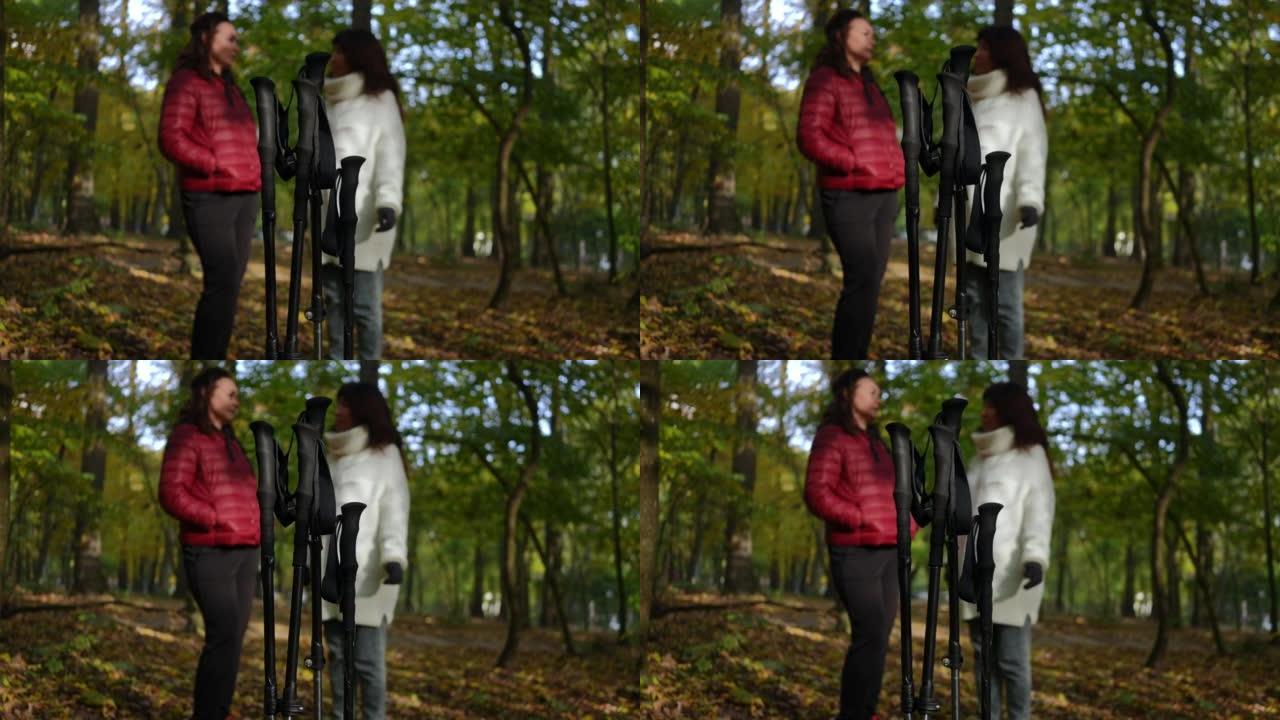 北欧人在森林中行走的特写杆，背景是模糊的成熟女性。自信的高加索朋友聊天分享谣言站在户外秋季公园训练休
