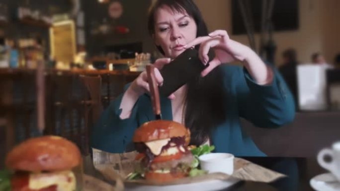 一名妇女在社交网络咖啡馆的桌子上的智能手机上拍摄了美味汉堡的照片。