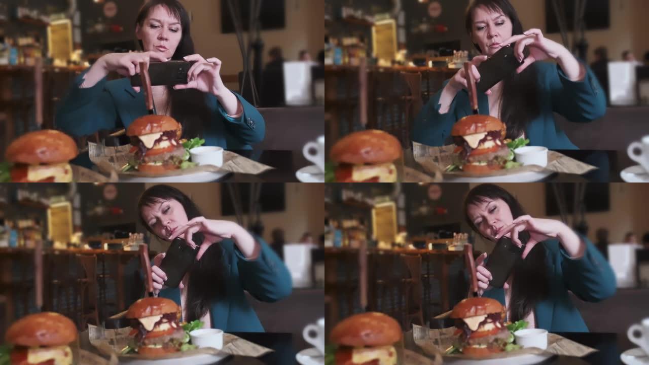 一名妇女在社交网络咖啡馆的桌子上的智能手机上拍摄了美味汉堡的照片。