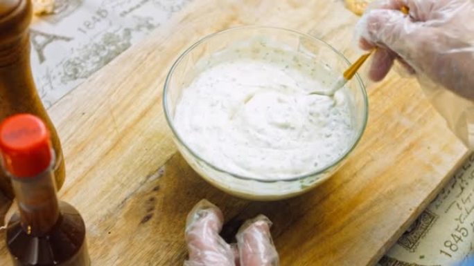 厨师将酸奶与酸奶油和蛋黄酱混合到牧场酱的配料中。使用金勺